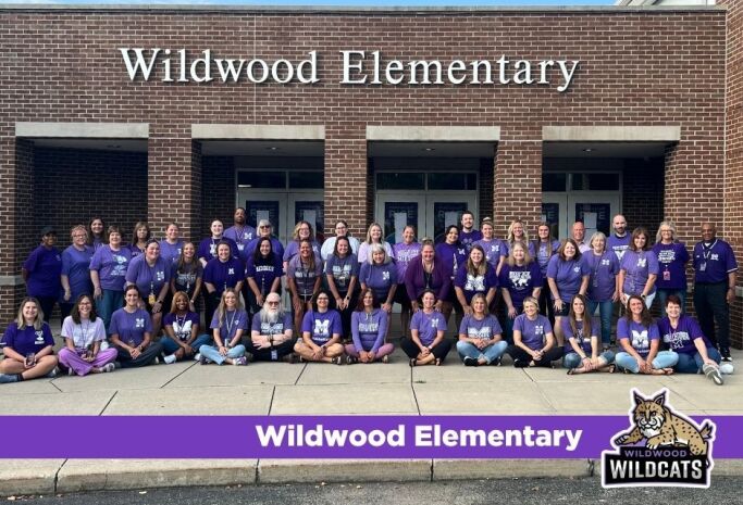 staff photo in front of school building with wildcats logo and school name